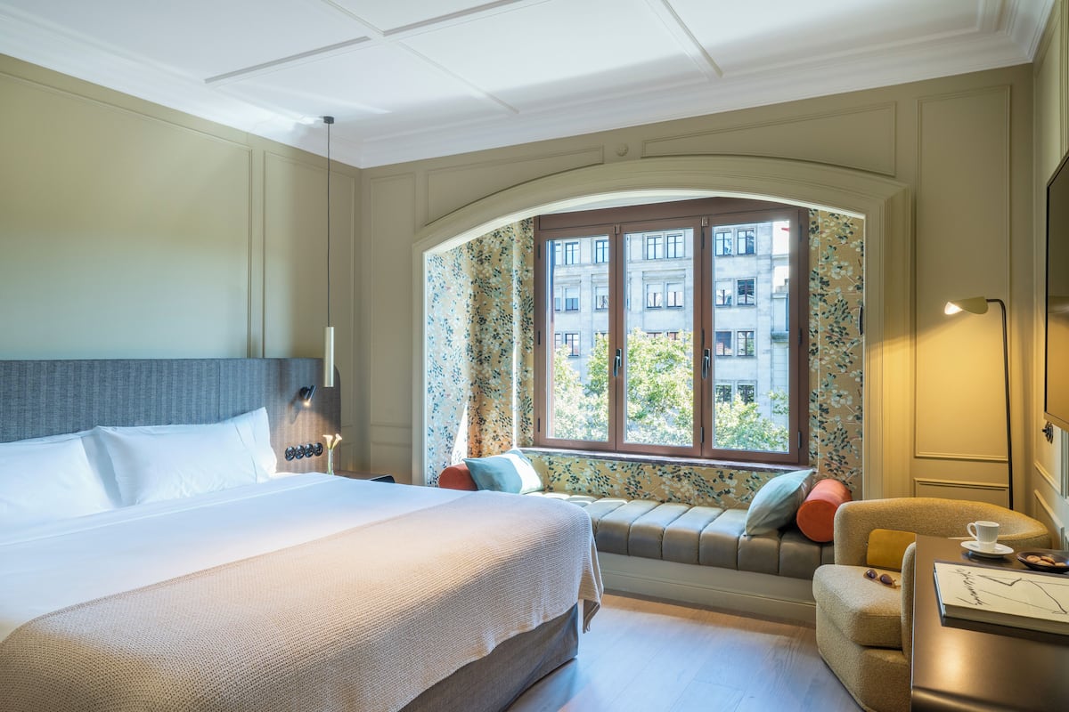 Une chambre d’hôtel avec un grand lit, un coin salon près de la fenêtre et un bureau avec une lampe.