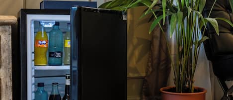 A refrigerator with beverages inside, a potted plant beside it, and a chair in the background.