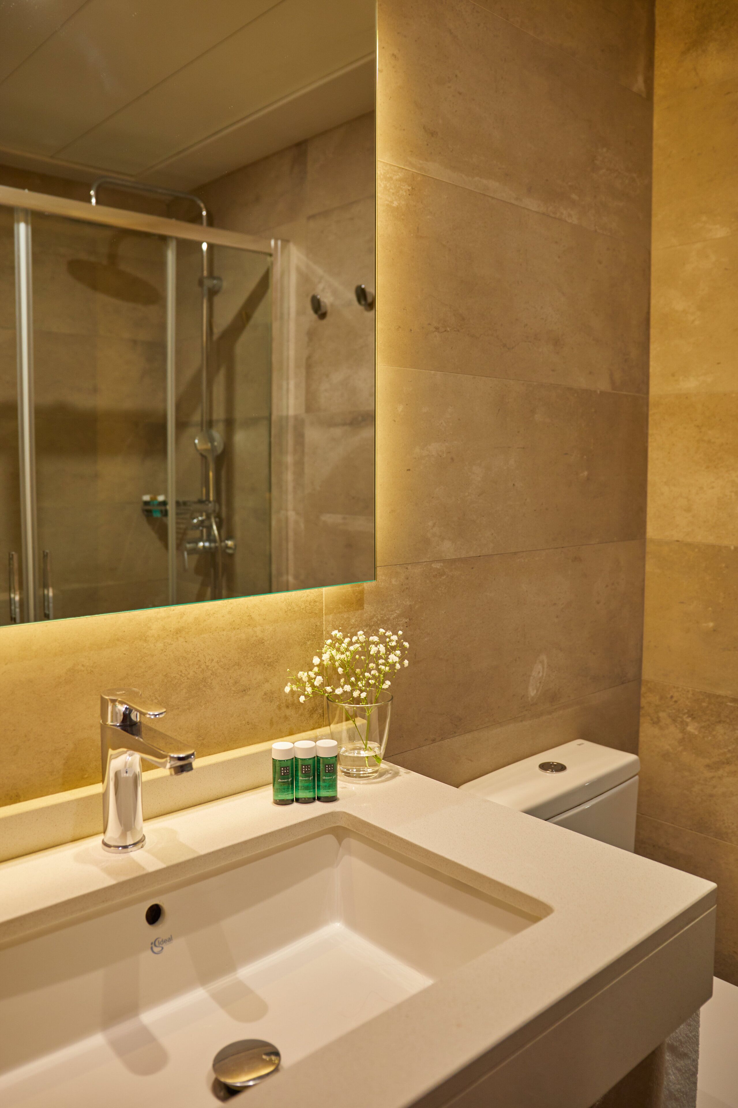 A bathroom with a large mirror, a sink, a glass shower enclosure, and toiletries on the counter.