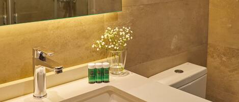 A bathroom with a large mirror, a sink, a glass shower enclosure, and toiletries on the counter.