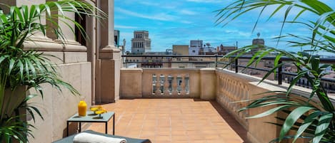 Terraço no telhado com vista para prédios da cidade, uma mesa com bebida e cadeiras de descanso.