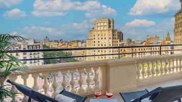 Un balcón con mesa y sillas, con vista a un paisaje urbano y edificios históricos.