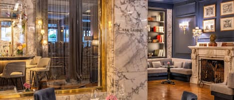 A luxurious interior with a marble column labeled "Casa Levene 1975," a dining area with a round table, and a cozy seating area with a fireplace.