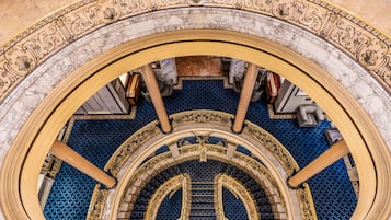 A grand staircase with marble and blue patterned flooring, surrounded by ornate golden railings.