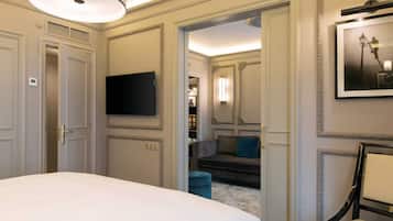Habitación de hotel con una cama grande, un televisor de pantalla plana montado en la pared, un sofá en la habitación contigua y un cuadro enmarcado en la pared.