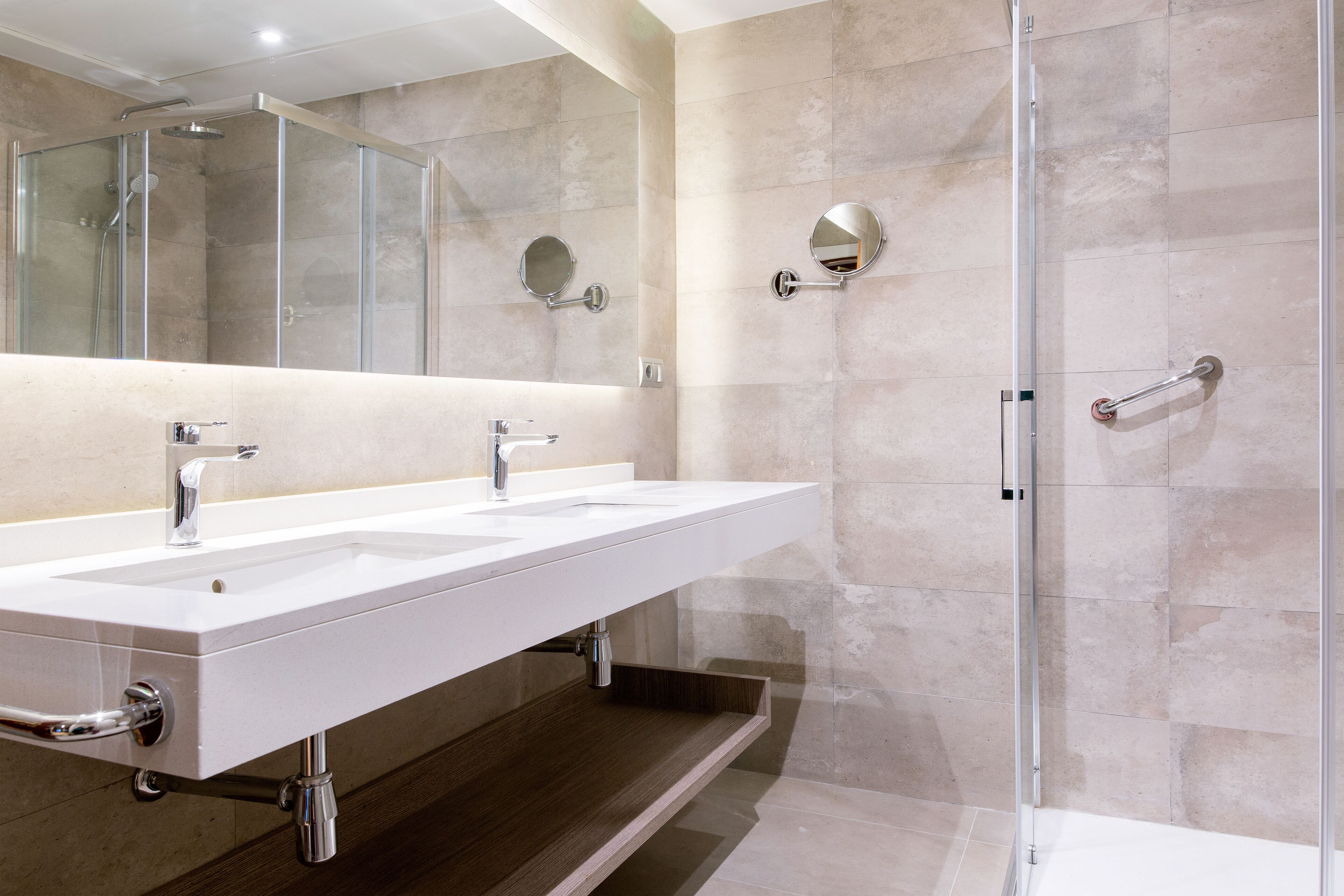 A modern bathroom with a double sink, a glass-enclosed shower, and a large mirror.