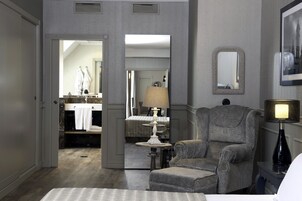 A hotel room with a bed, a chair, a lamp, a mirror, and a bathroom visible through an open door.