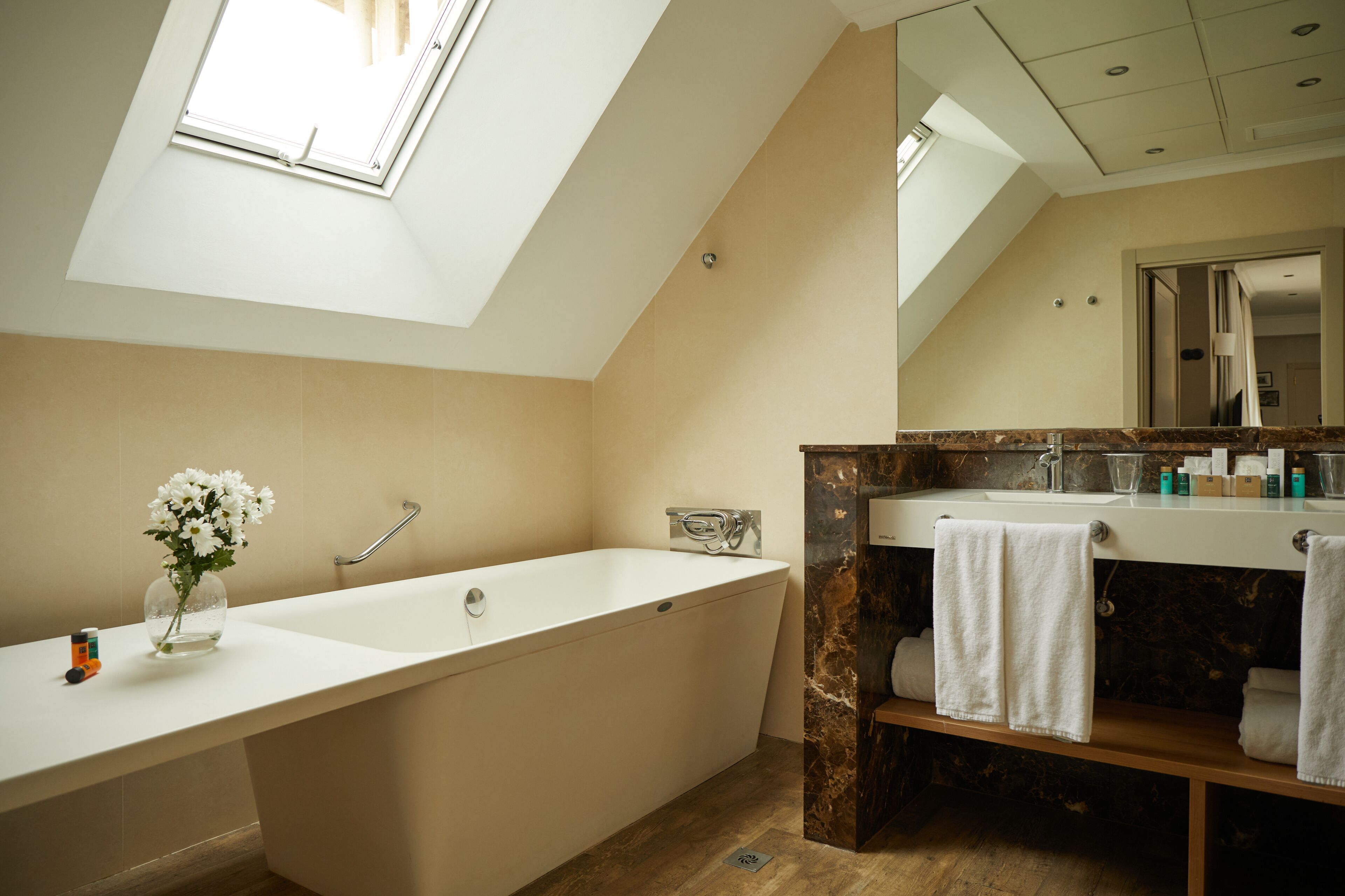A modern bathroom with a skylight, a freestanding bathtub, a marble vanity, and a large mirror.