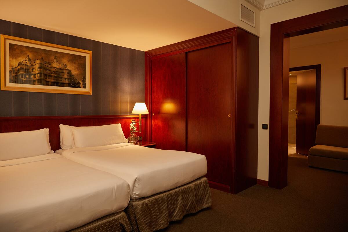 Une chambre d’hôtel avec deux lits, une armoire en bois, un tableau encadré au mur et une lampe sur la table de chevet.