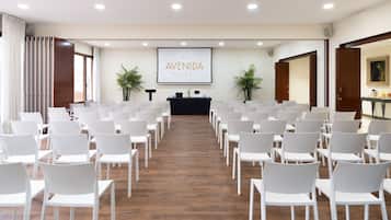 Un salón de conferencias con hileras de sillas blancas, un atril y una pantalla de proyector que muestra