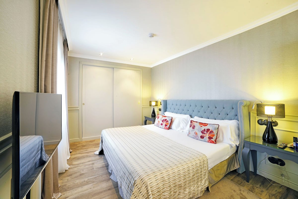 Une chambre d’hôtel avec un grand lit, deux tables de chevet avec des lampes, une télévision et une armoire.