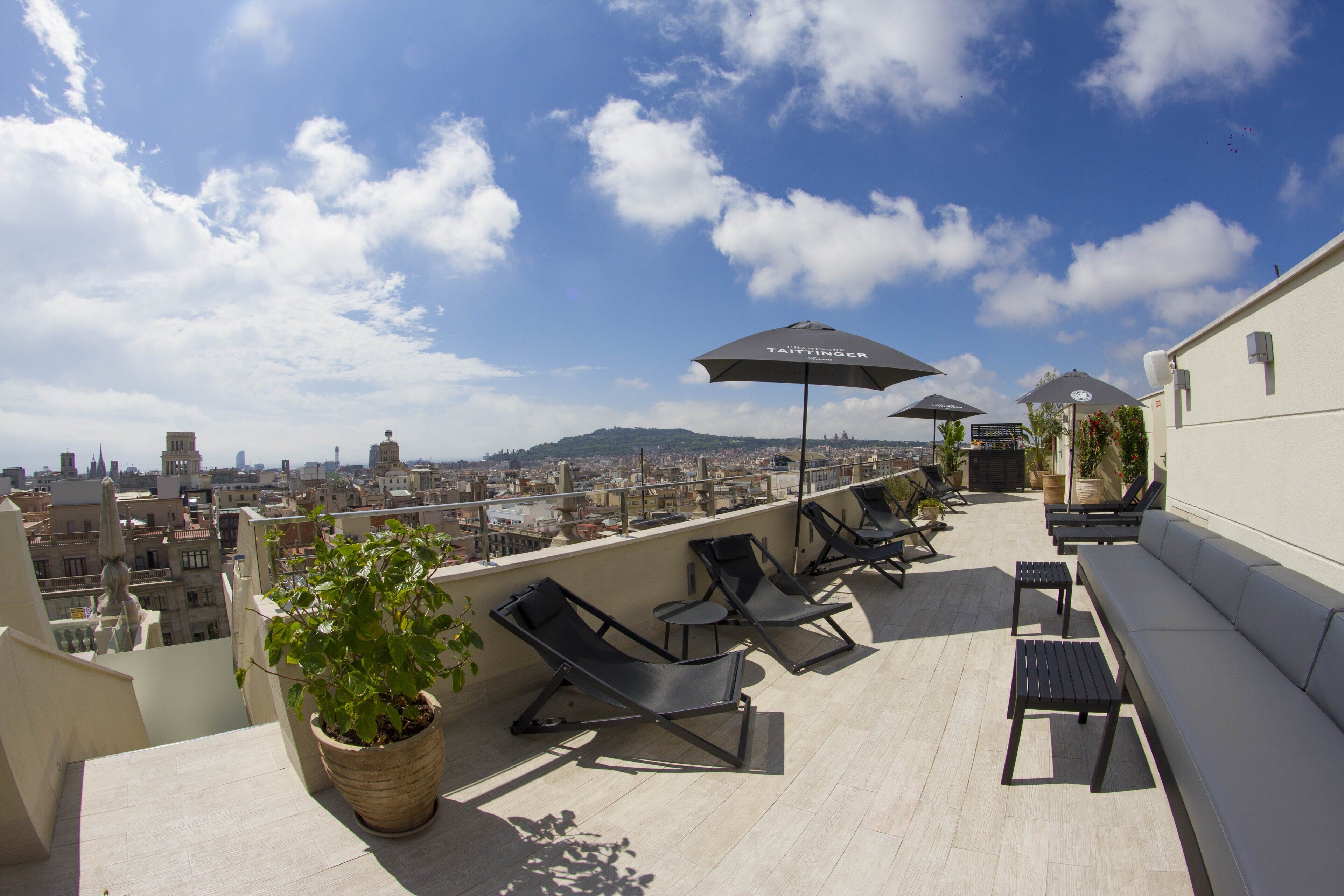 Una terraza en la azotea con sillones de descanso, una planta en maceta y sombrillas.