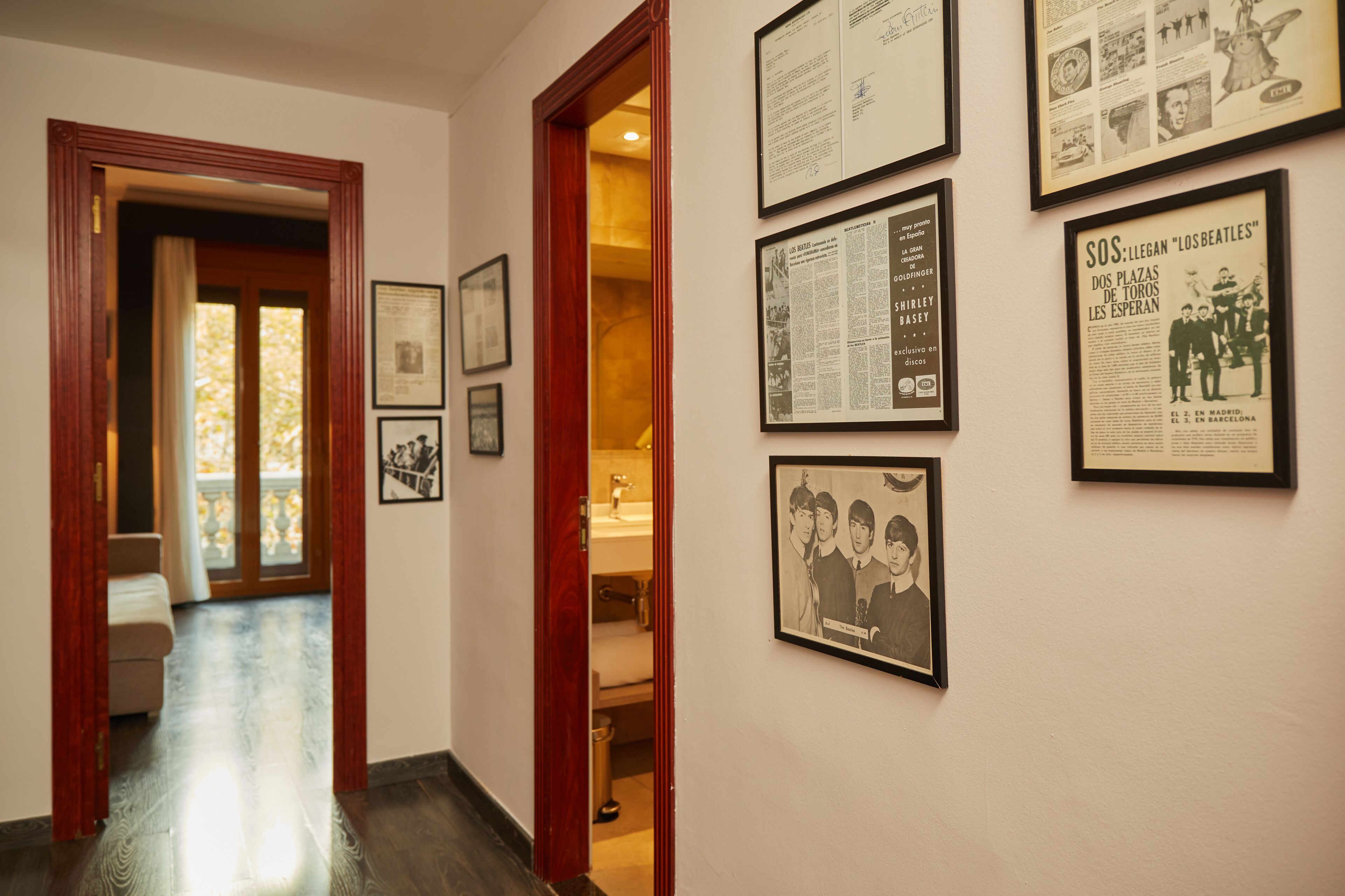 A hallway with framed historical documents and photographs on the walls, leading to a room with a wooden door and a visible bathroom.