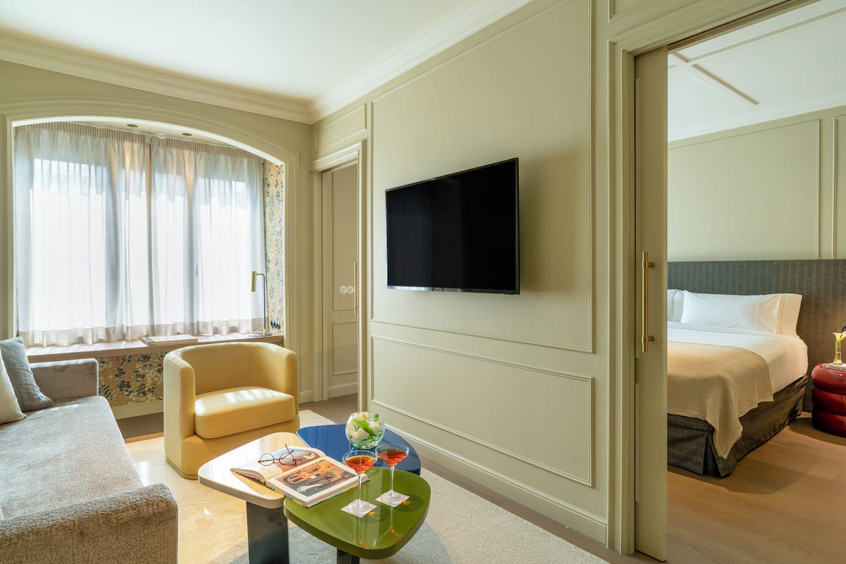 Une chambre d’hôtel équipée d’un lit, d’une télévision, d’un canapé et d’une table basse avec un magazine et des verres.