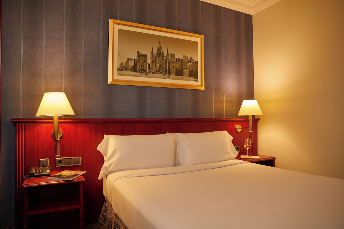 Une chambre d’hôtel avec un grand lit, deux tables de chevet, un tableau encadré au mur et deux lampes.