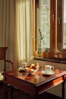 Une table en bois sur laquelle se trouve un panier de croissants et deux tasses blanches, une plante en pot et une fenêtre avec des rideaux.