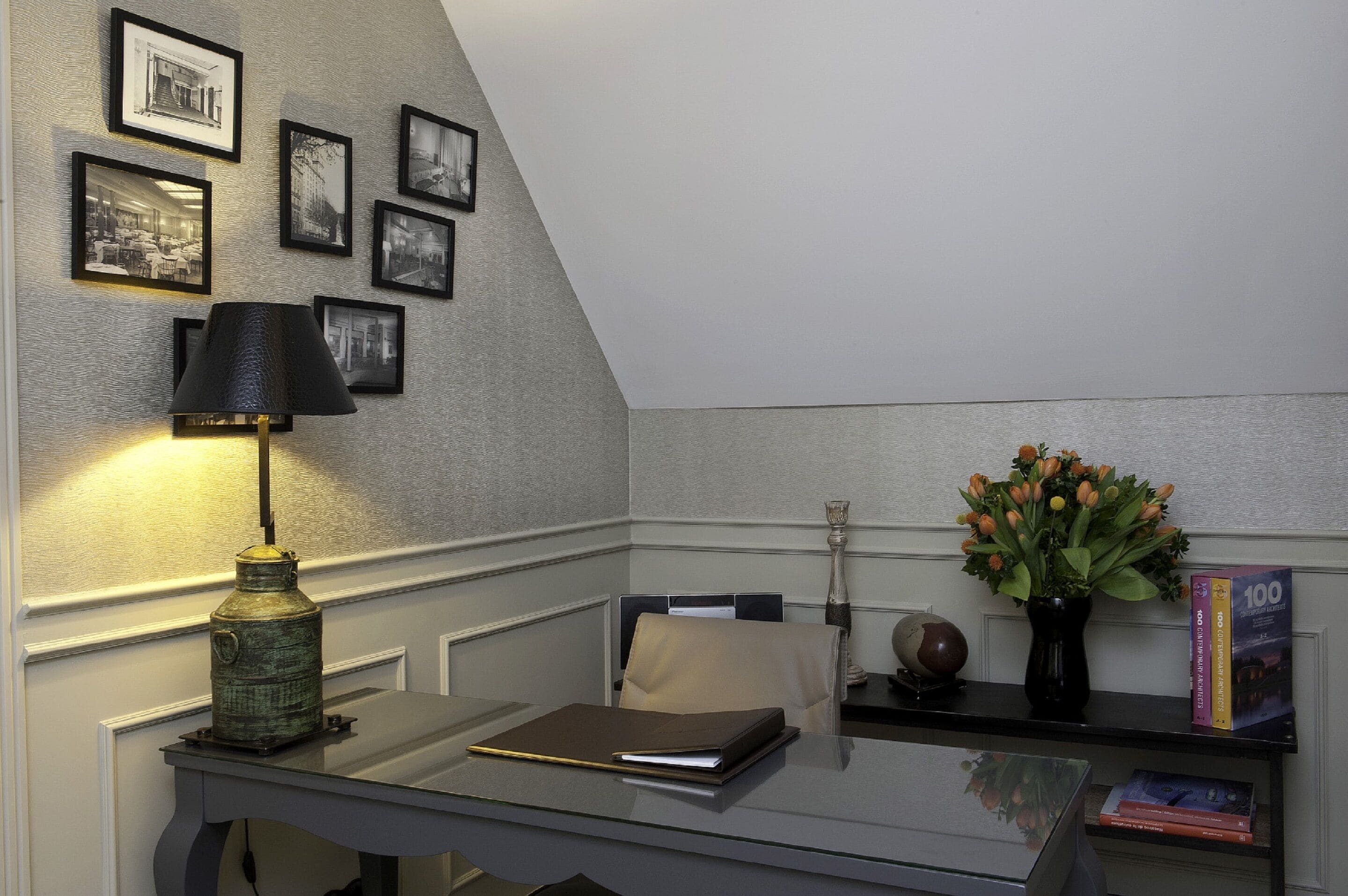 Un bureau d’angle avec un bureau, une lampe, des photos encadrées, un vase avec des fleurs et des livres.