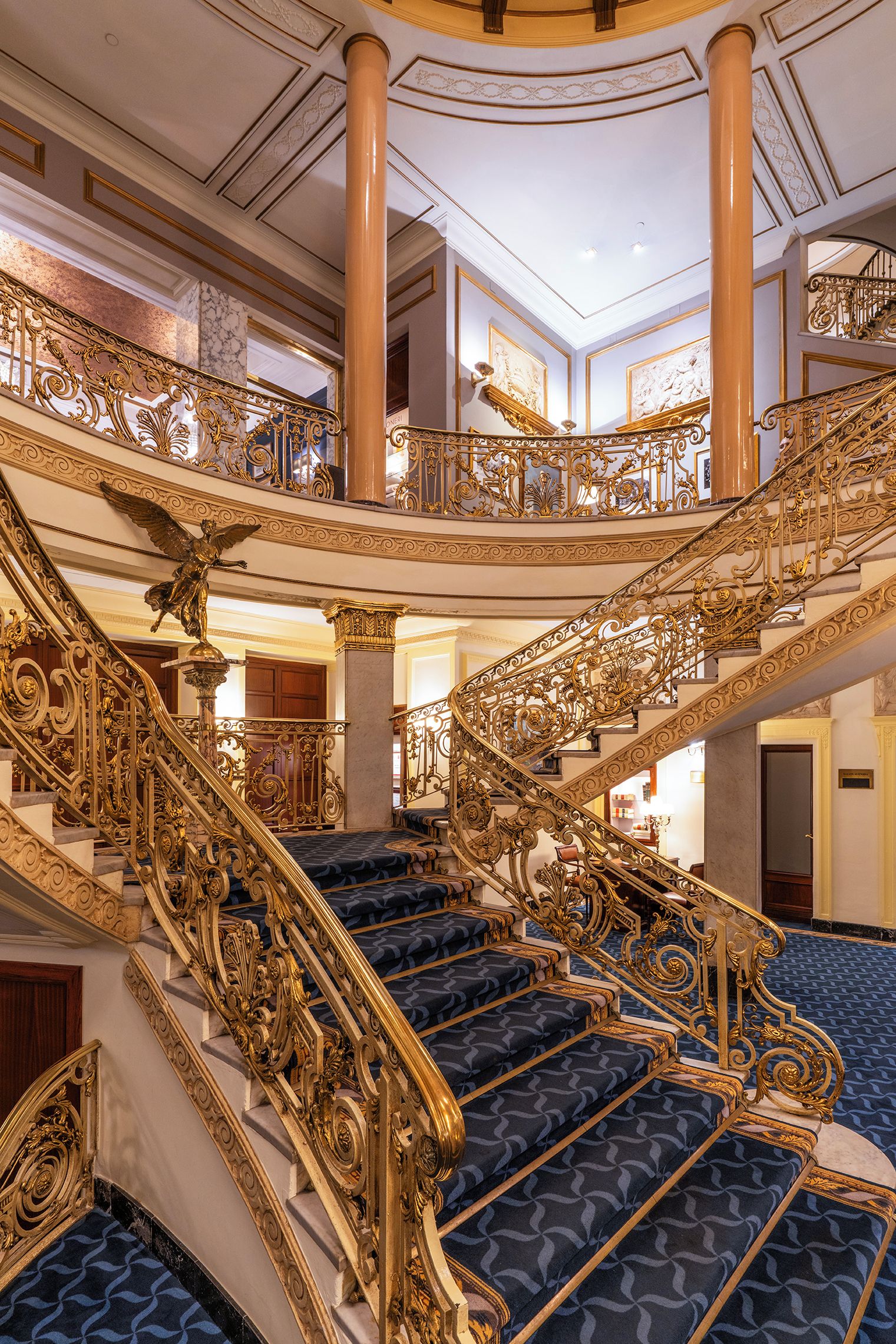 Eine prächtige, verzierte Treppe mit aufwendigen, goldenen Geländern und einem teppichartigen Belag mit blauem Muster.
