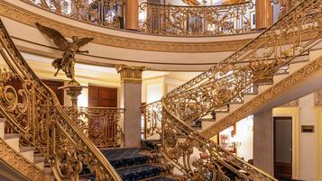Eine prächtige, verzierte Treppe mit aufwendigen, goldenen Geländern und einem teppichartigen Belag mit blauem Muster.