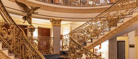 Una imponente escalera con ornamentadas barandillas doradas y alfombra de estampado azul.