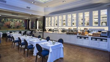 Uma sala de jantar com mesas preparadas para o serviço, um buffet com diversos alimentos e um quadro grande na parede.