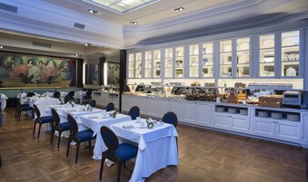 Uma sala de jantar com mesas preparadas para o serviço, um buffet com diversos alimentos e um quadro grande na parede.