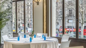 Un coin repas avec une table ronde dressée pour quatre personnes, de grandes fenêtres offrant une vue sur la ville et un lustre.