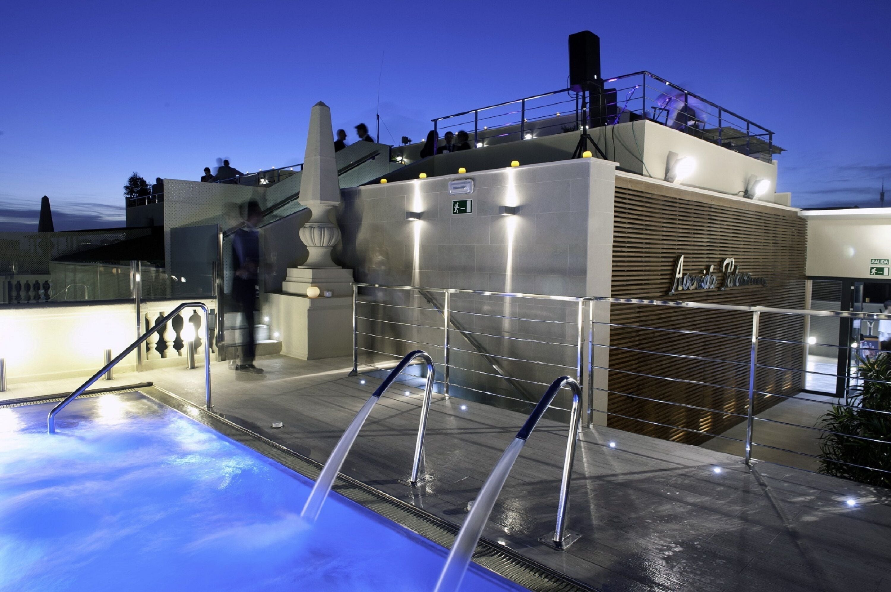 Un área de piscina en la azotea con un jacuzzi, escaleras y vistas a la ciudad al atardecer.