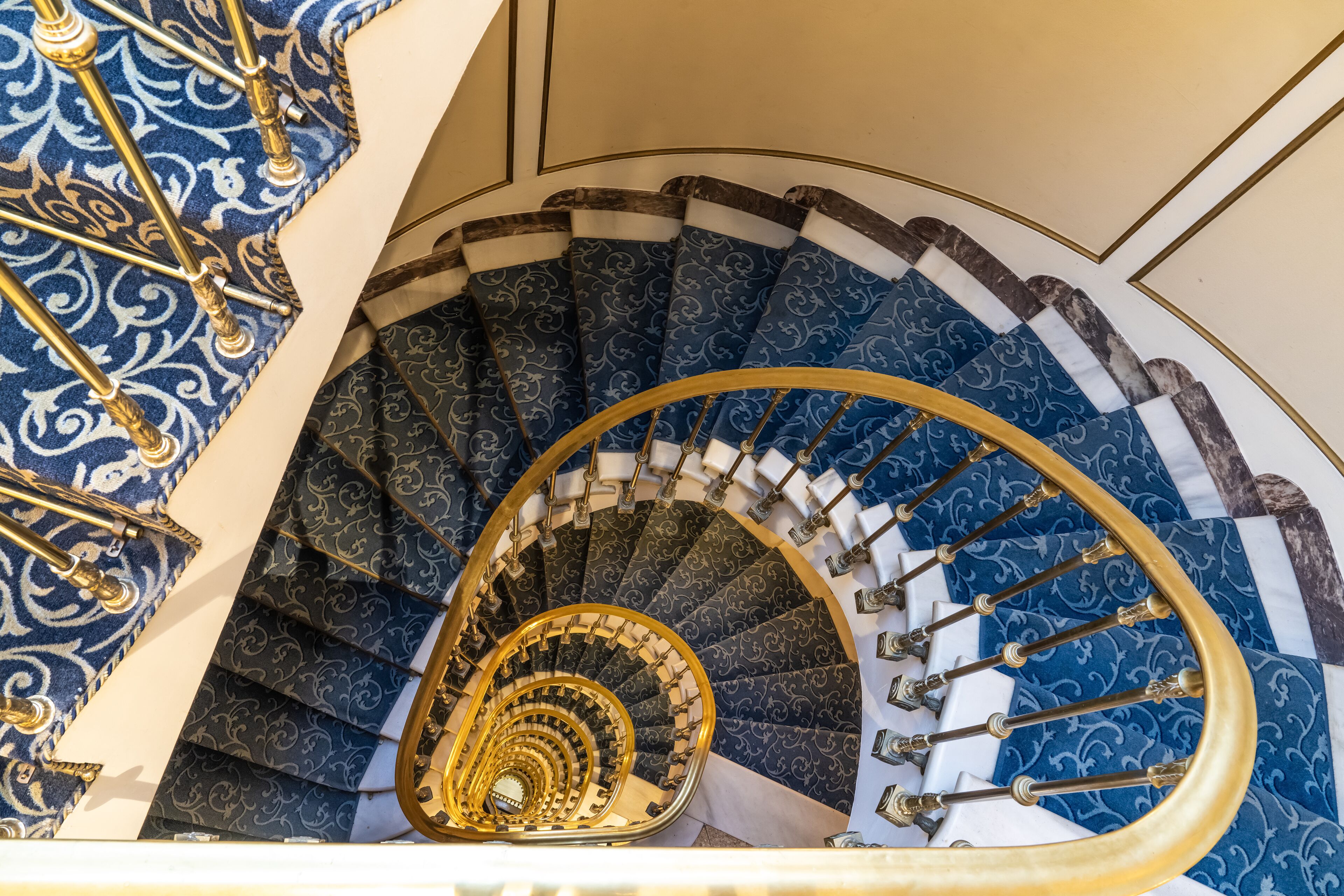 A grand spiral staircase with ornate blue and gold railings and a marble finish.