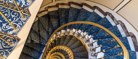 A grand spiral staircase with ornate blue and gold railings and a marble finish.