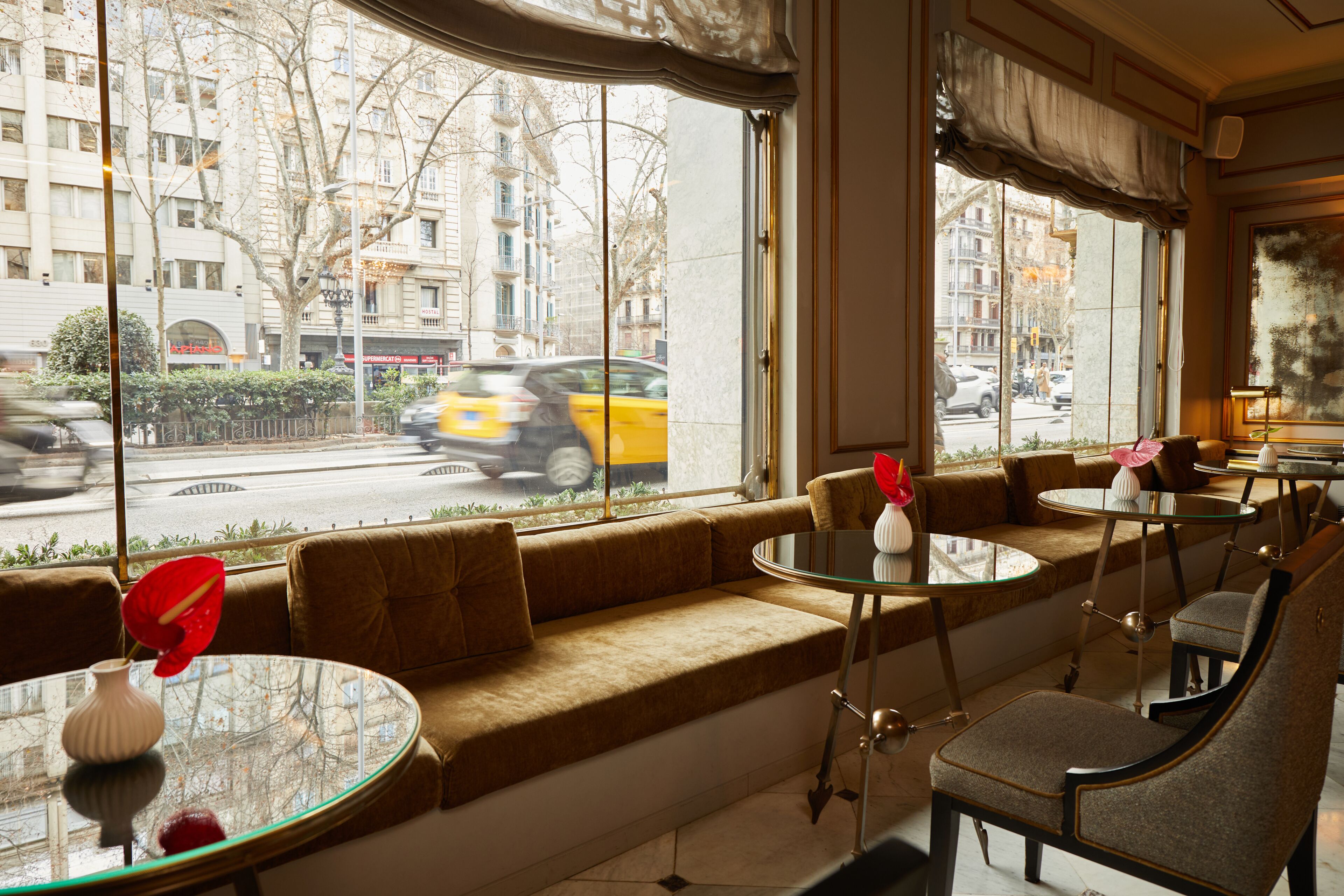 A cozy seating area with a sofa and tables, large windows with a view of the street, and a lamp on the table.