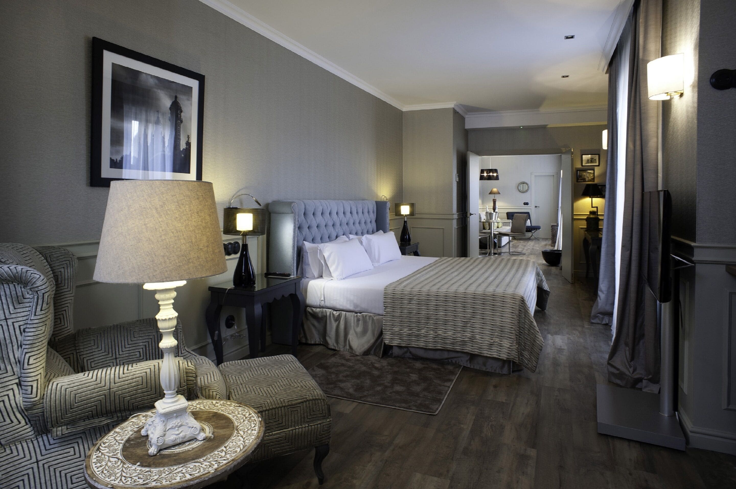 A hotel room with a large bed, two bedside tables, a chair, and a small round table with a lamp.