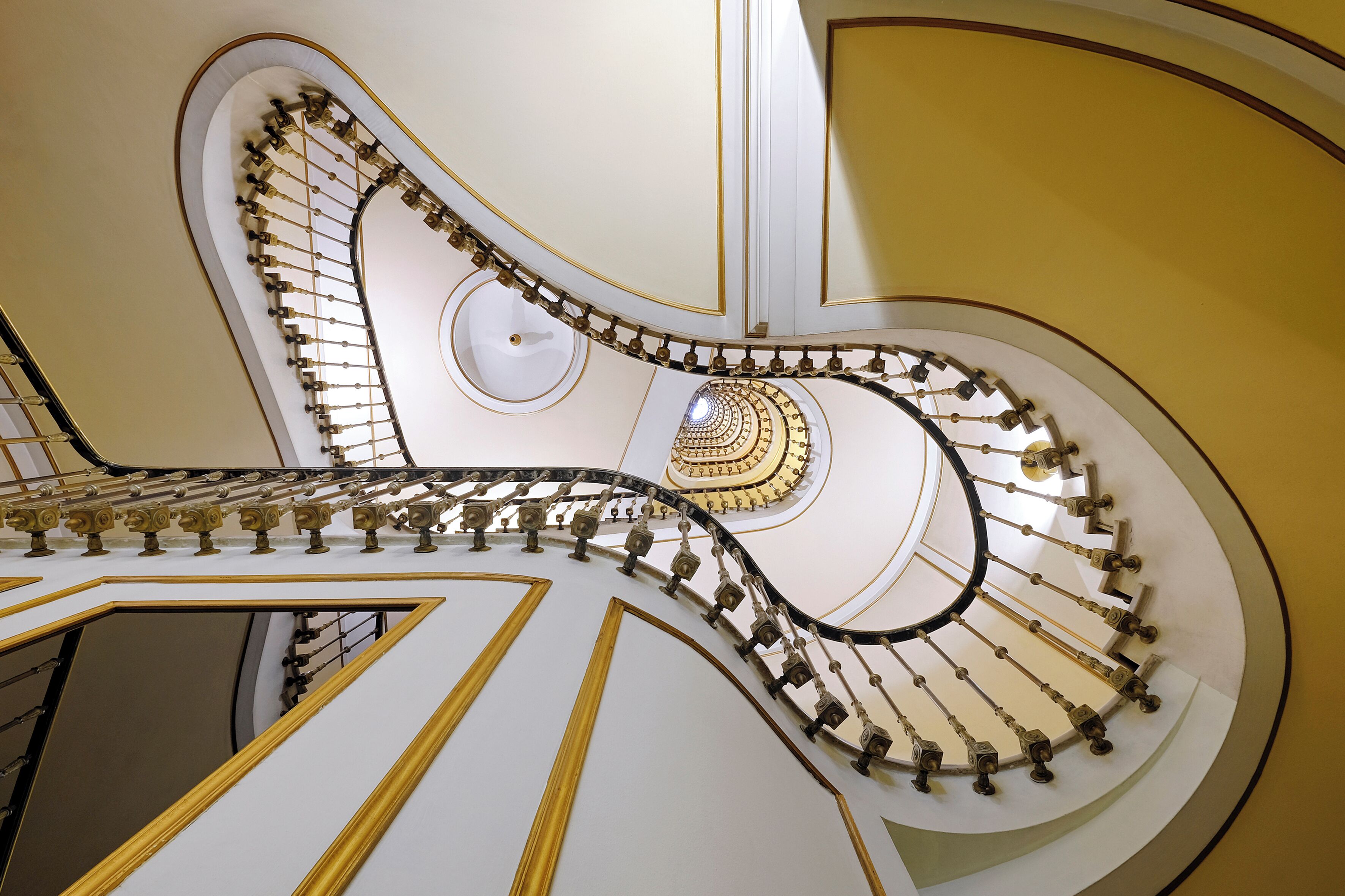 Eine prächtige Wendeltreppe mit aufwendiger Goldverzierung und weißen Wänden.