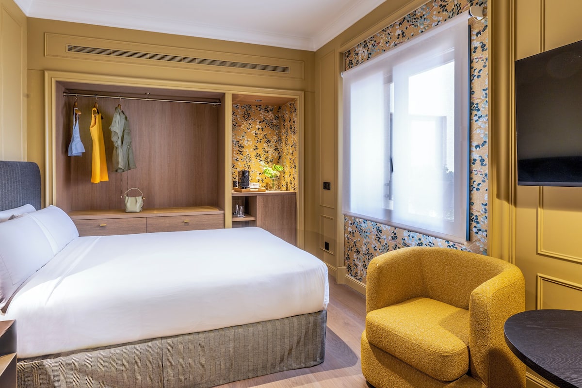 Une chambre d’hôtel avec un grand lit, une armoire, une petite table, une chaise et un téléviseur.