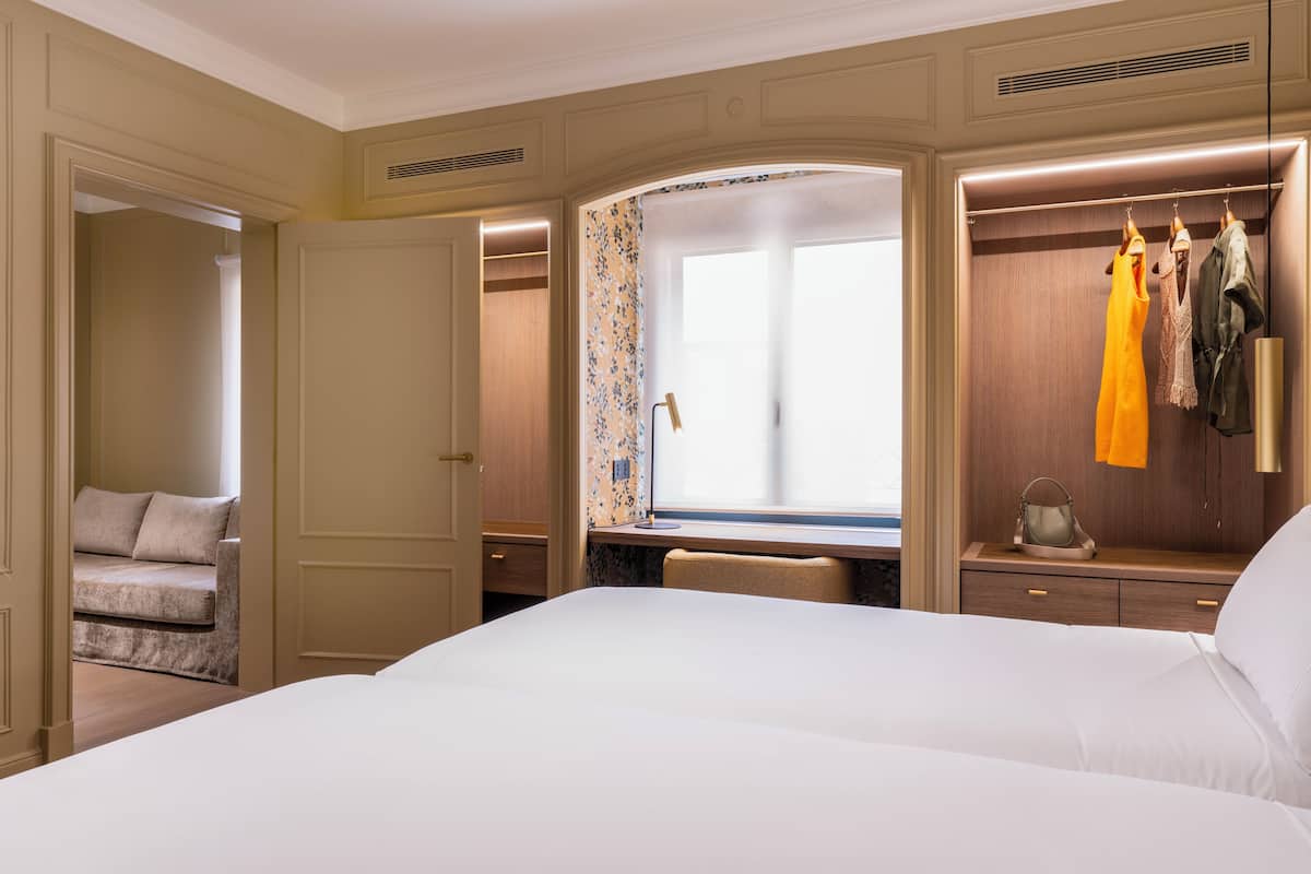 Une chambre d’hôtel dotée d’un grand lit, d’un coin salon avec un canapé, d’un bureau avec une chaise, d’une armoire et d’une fenêtre avec des rideaux.