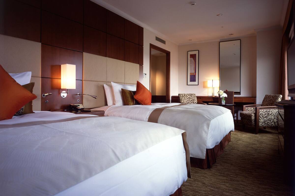 A hotel room with two beds, a desk, a chair, a mirror, and a carpeted floor.