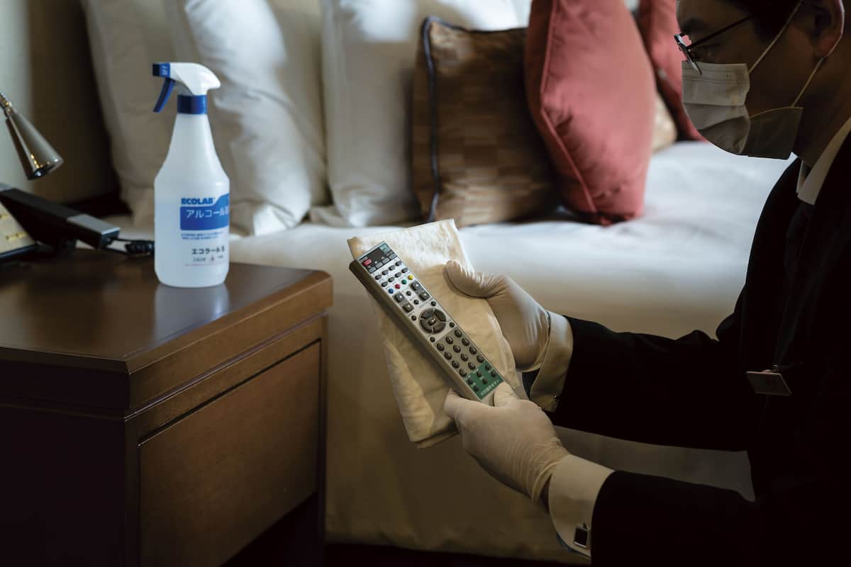 A hotel room with a remote control, a spray bottle, and a pillow on the bed.