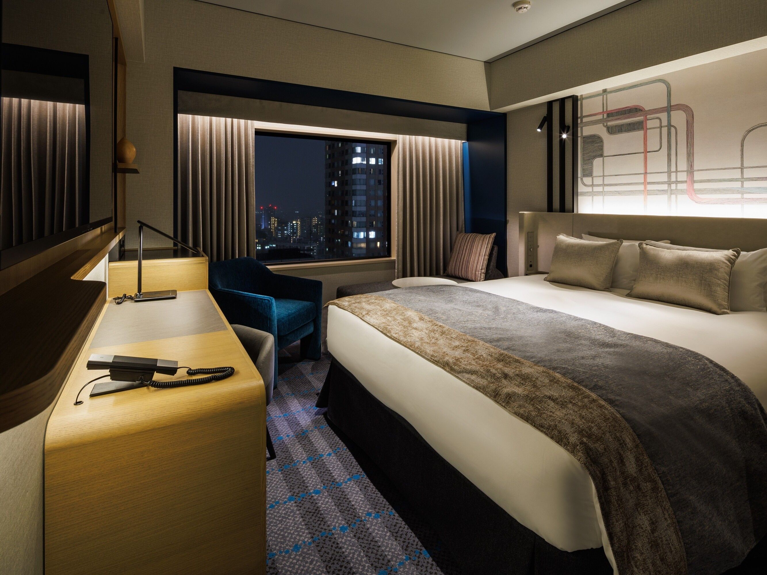 A hotel room with a bed, a desk, a chair, and a window with a city view.