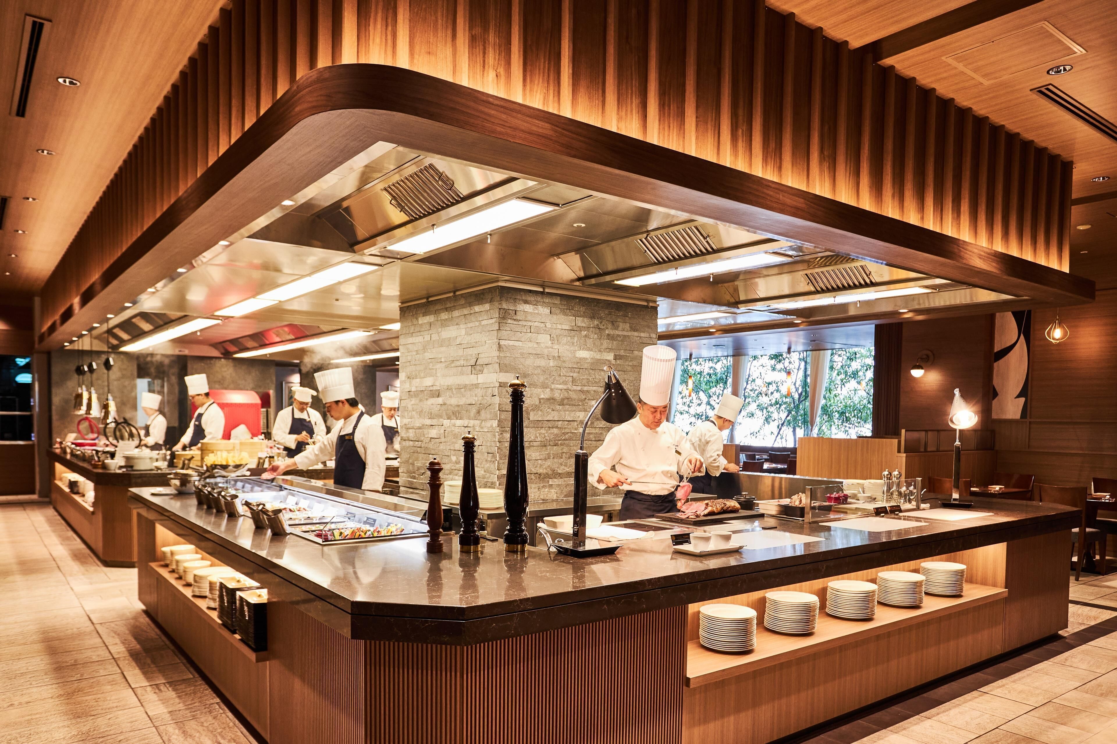 A modern kitchen with chefs preparing food, a central island with dishes, and a wooden ceiling design.