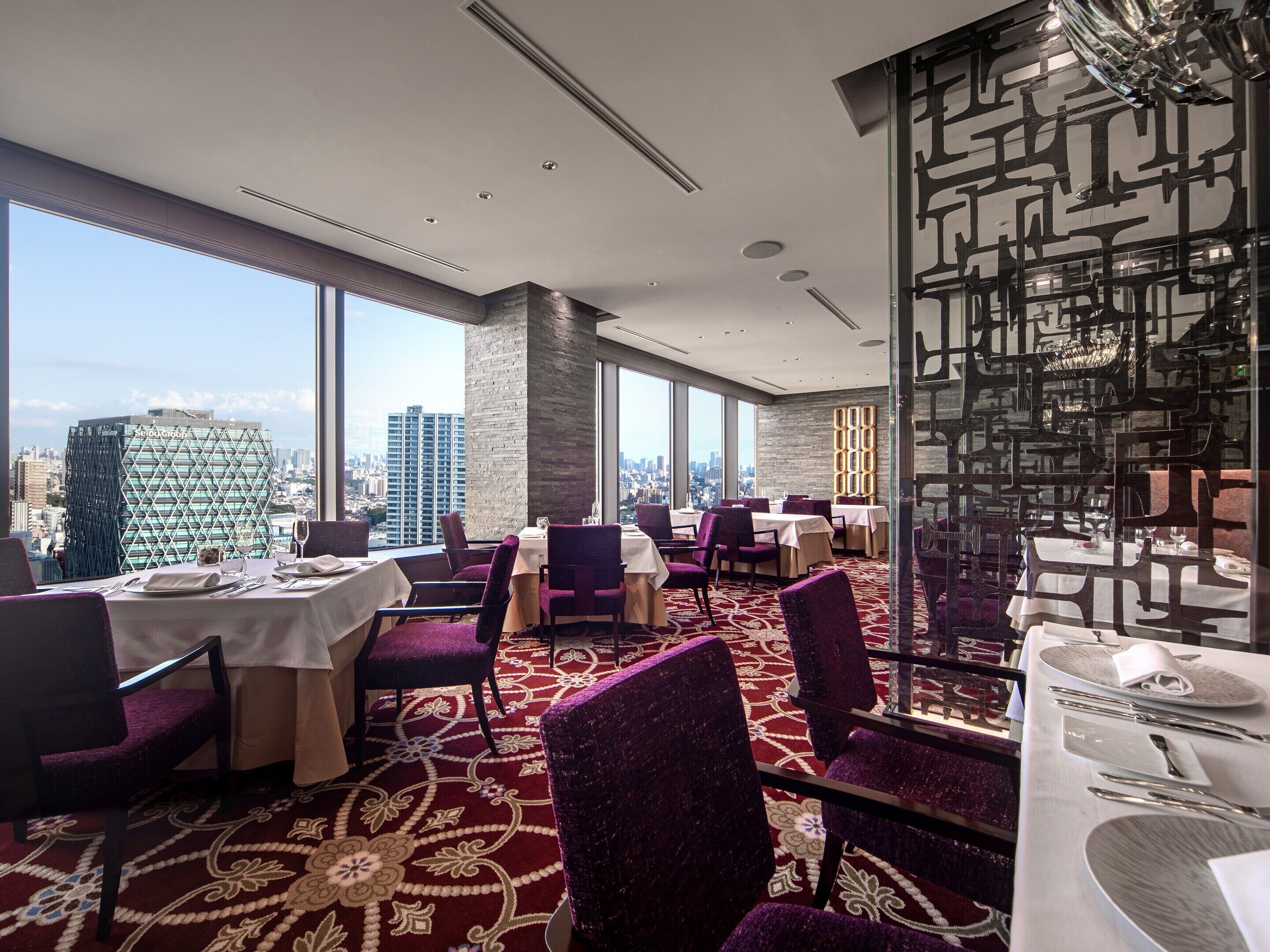 A high-rise restaurant with tables set for dining, large windows offering city views, and a modern interior design.