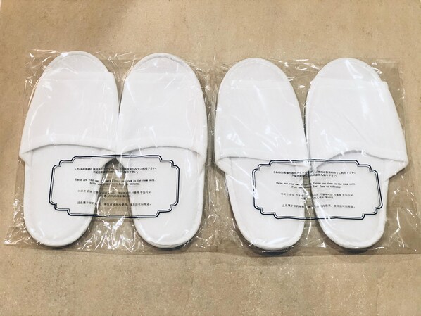 A pair of white slippers in plastic packaging with a label. - Hotel Metropolitan Tokyo Ikebukuro (Tokyo)