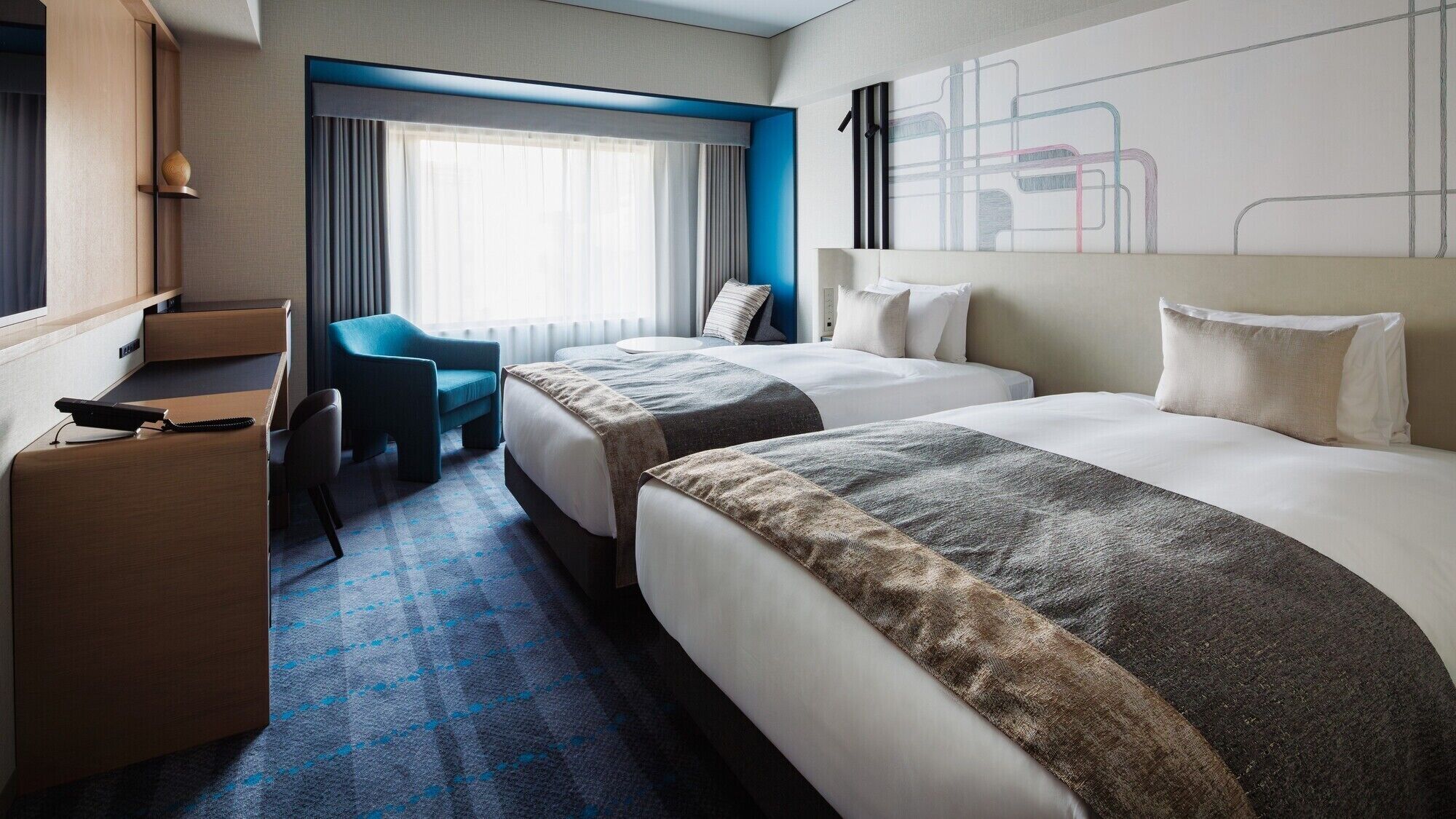 A hotel room with two beds, a desk, a chair, and a large window with curtains.
