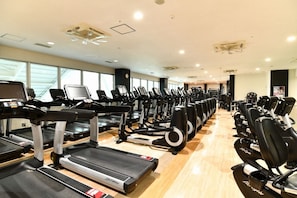 A gym with multiple treadmills and exercise bikes arranged in rows.