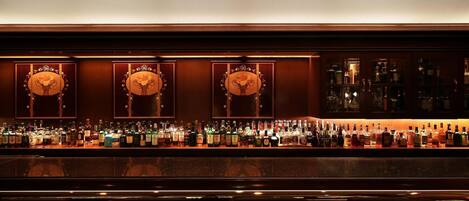 Un bar con una barra larga, varias botellas y tres paneles decorativos en la pared.