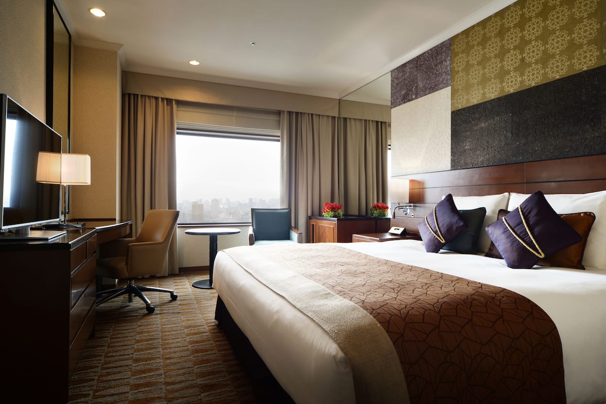 A hotel room with a large bed, a desk with a chair, a television, and a window with curtains.