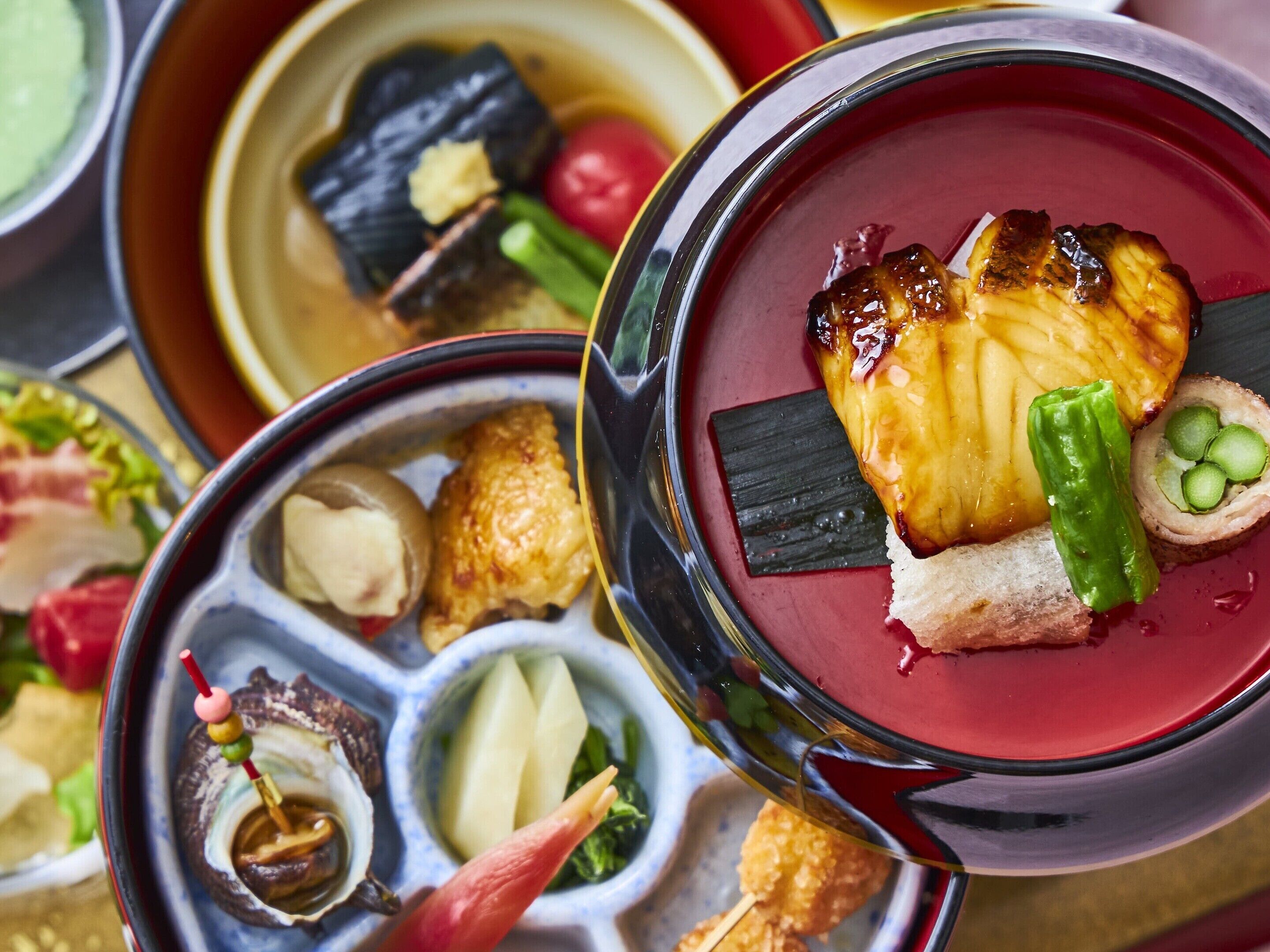 A variety of dishes in a dining setting, including a bowl with a red sauce and a piece of grilled meat.