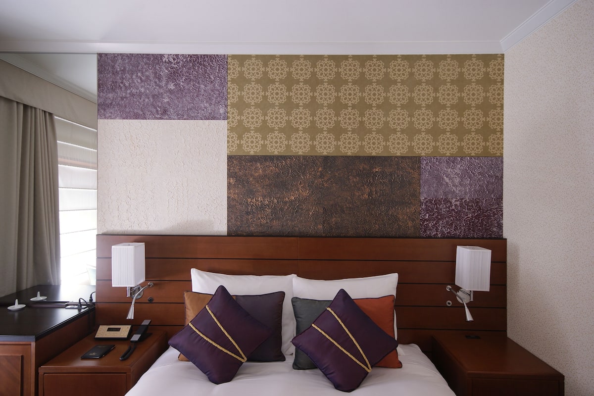 A hotel room with a wooden headboard, a bed with white bedding, and a nightstand with a lamp and a book.