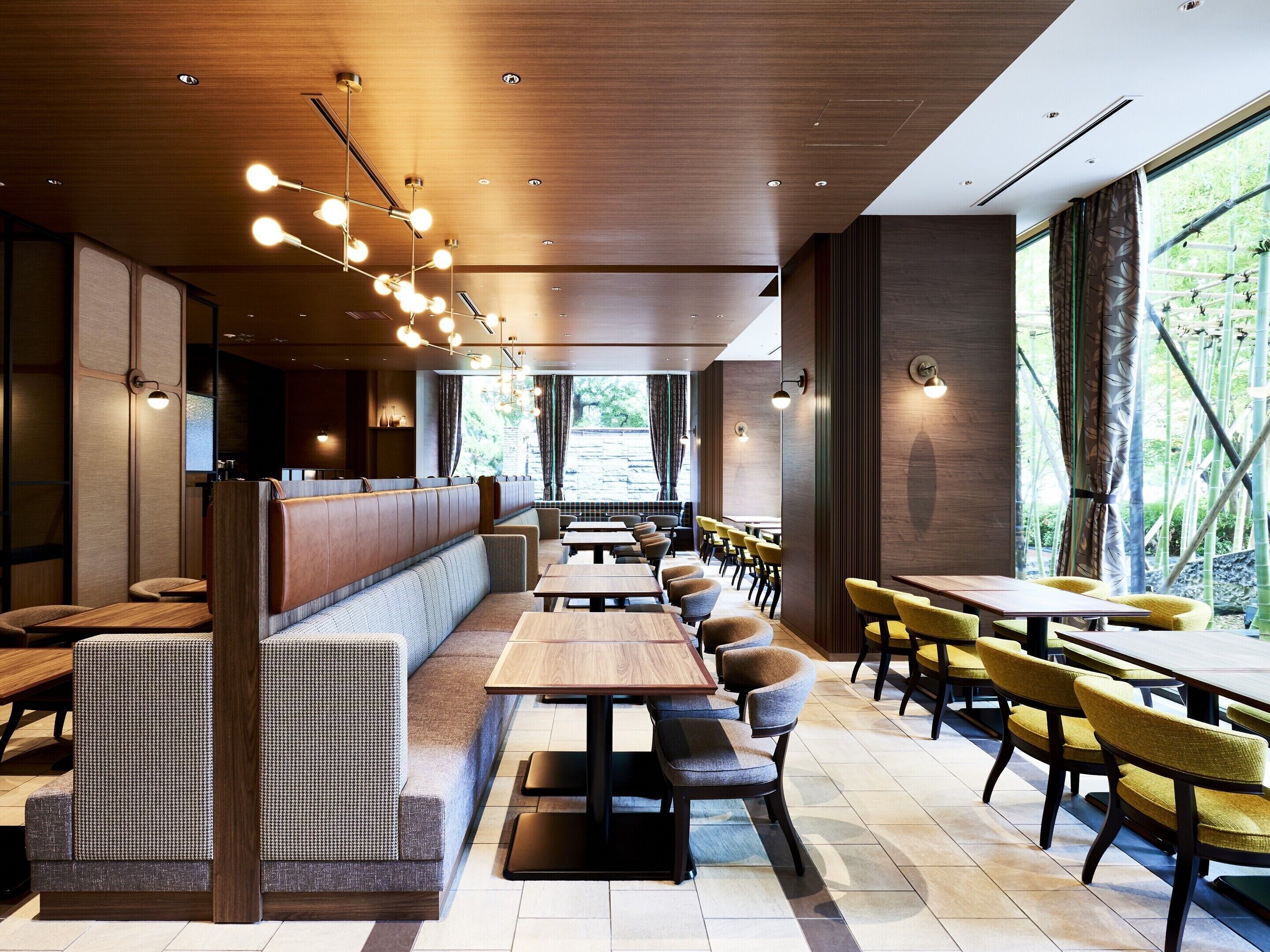 A modern restaurant interior with wooden paneling, tiered seating, and natural light from large windows.