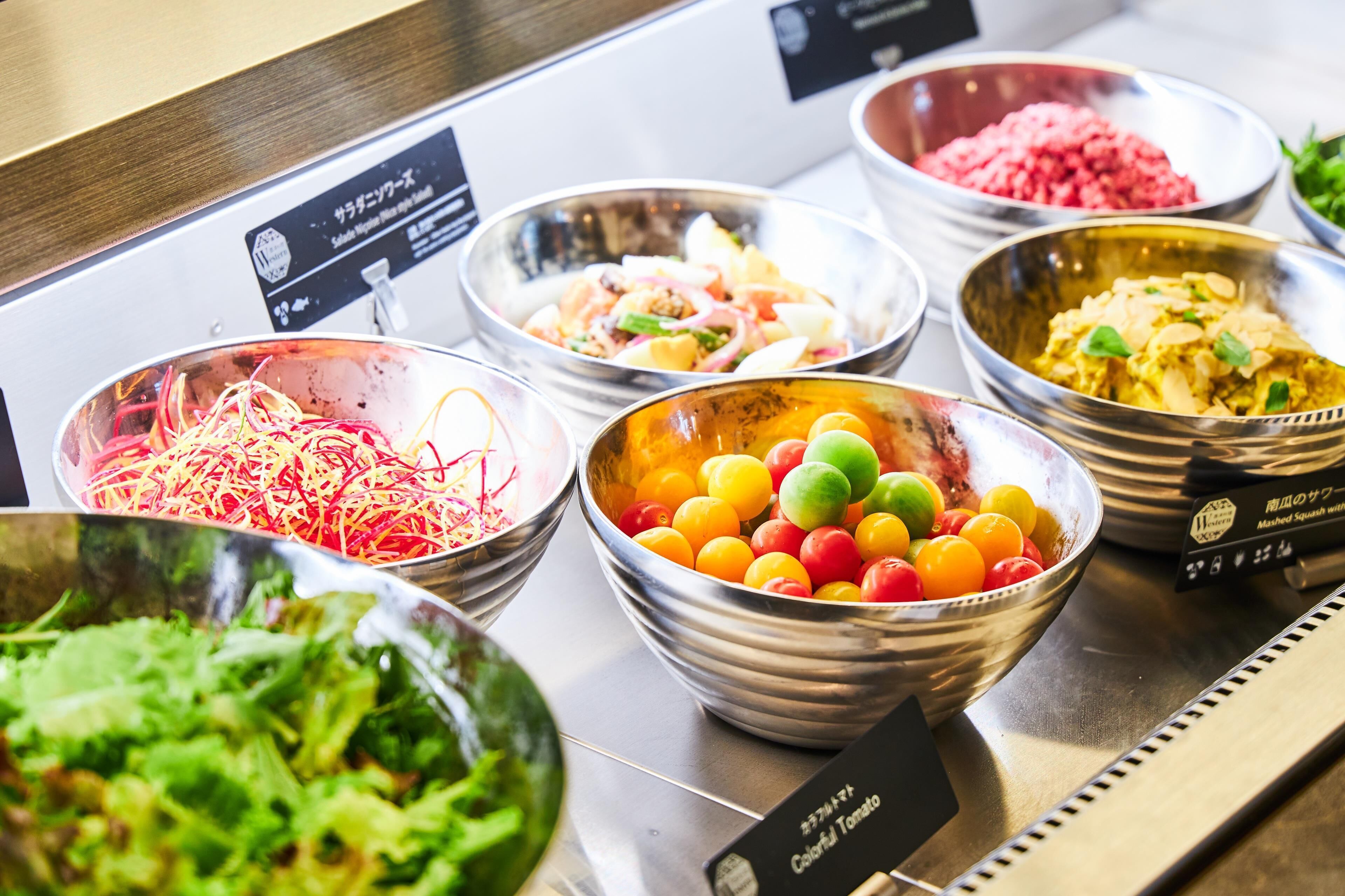 A buffet with various dishes including colorful tomatoes, shredded vegetables, and a salad.