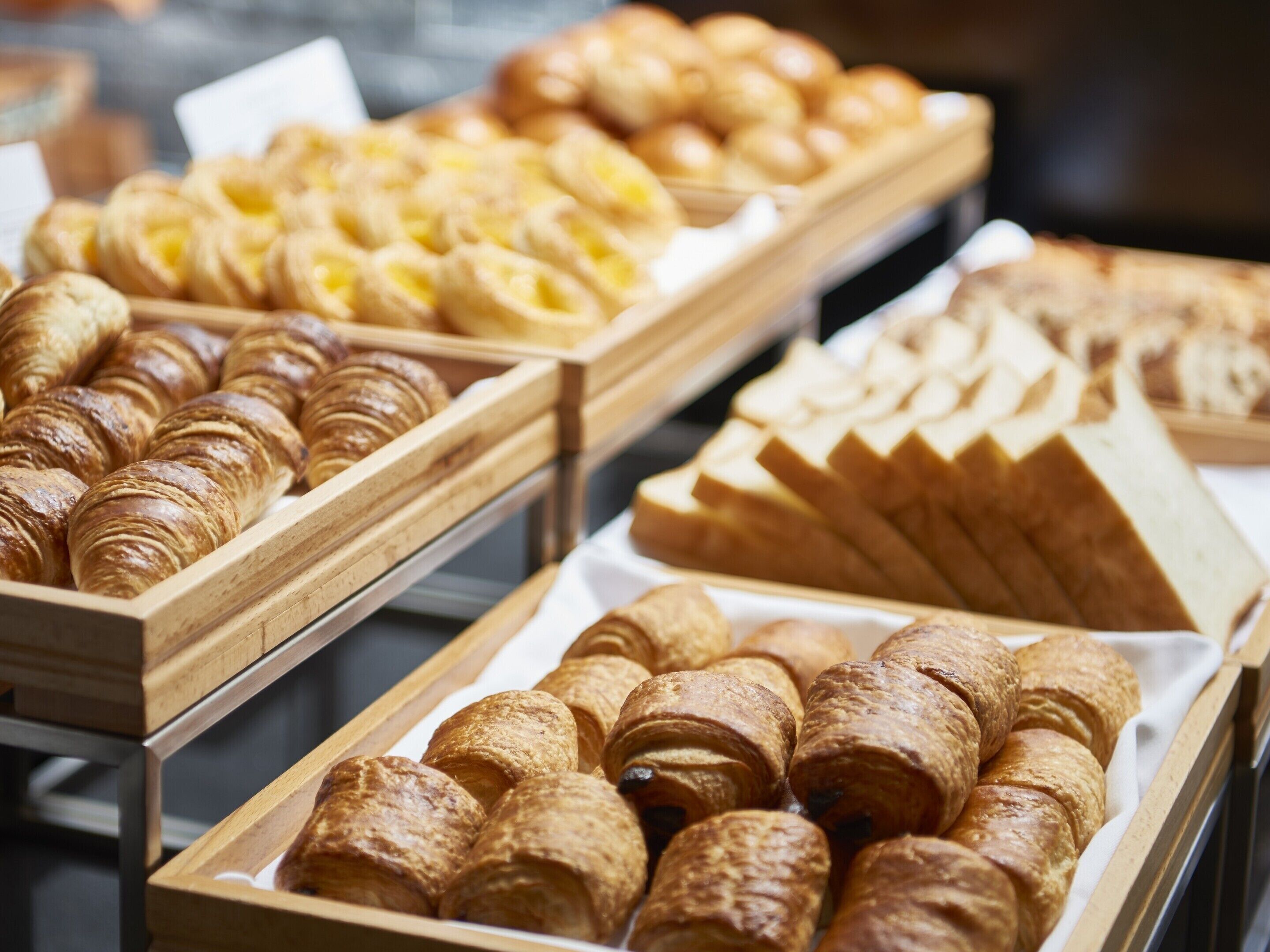 A display of various baked goods, including croissants and bread, arranged in wooden trays.